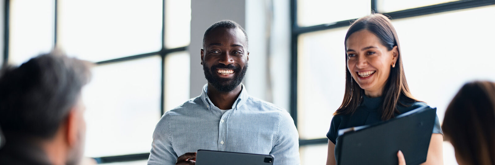 Man and woman on tablets smiling with other colleagues
